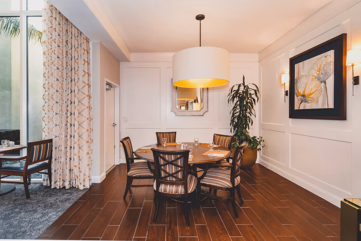 Round dining table with six striped chairs under a large pendant light in a well-decorated dining area with wall art and a potted plant.