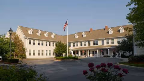 Exterior view of a two-story senior living facility with a driveway and flagpole.