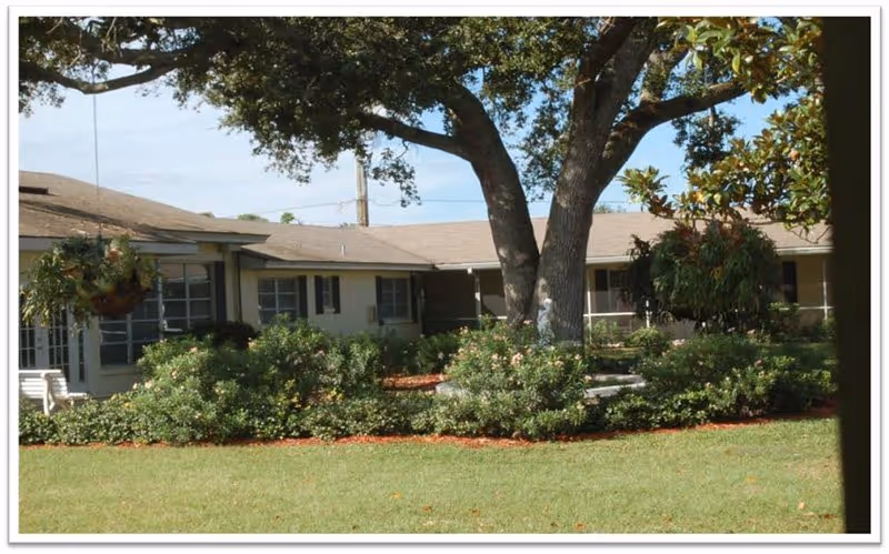 Courtyard with a large oak tree, trimmed shrubs and lawn in front of a single-story senior living building.