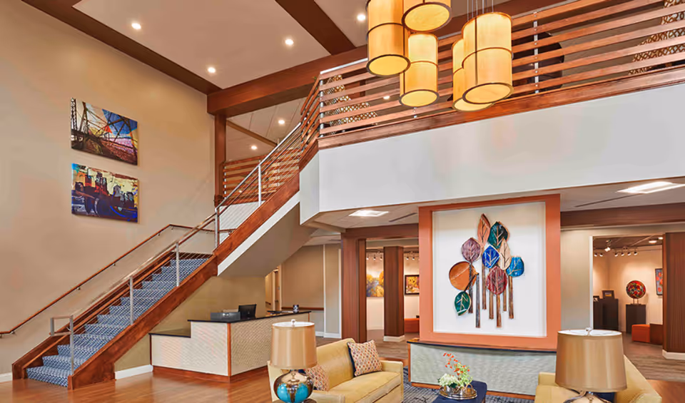 Spacious two-story lobby with a wooden staircase, seating area, pendant lights, and decorative wall art.