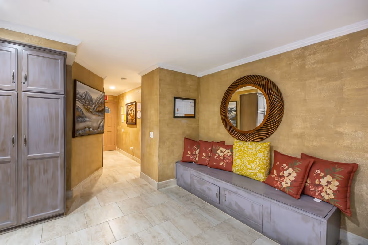 Hallway seating area with a built-in bench, floral pillows and a round mirror on a textured wall.