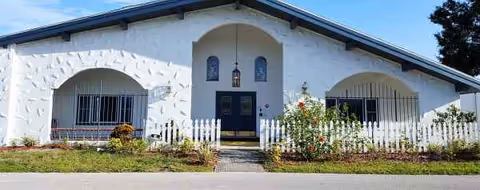 Single-story white facility building with arched windows, central door, and a small white picket fence.