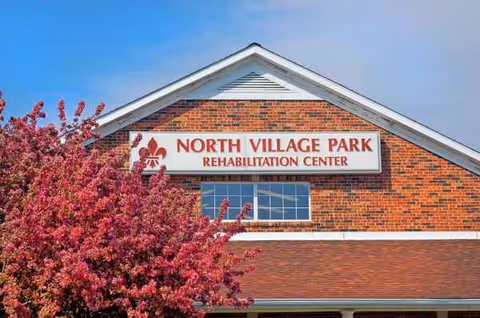 Brick building facade with North Village Park Rehabilitation Center sign and pink flowering tree.