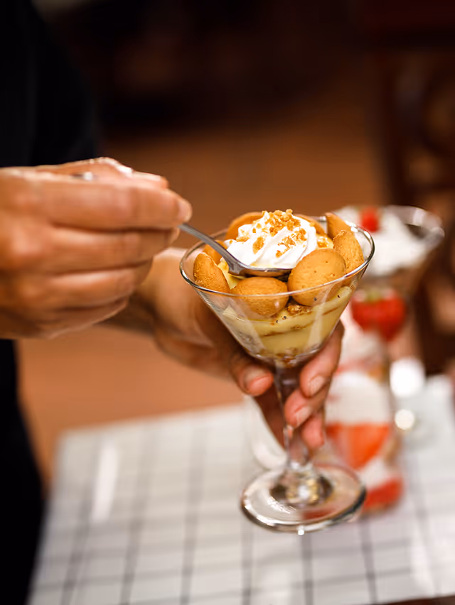 Hands holding a dessert parfait in a stemmed glass topped with whipped cream and cookies.