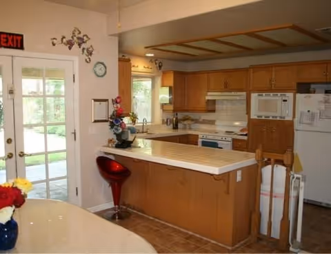 Bright kitchen with wooden cabinets, island, appliances, and an exit door.