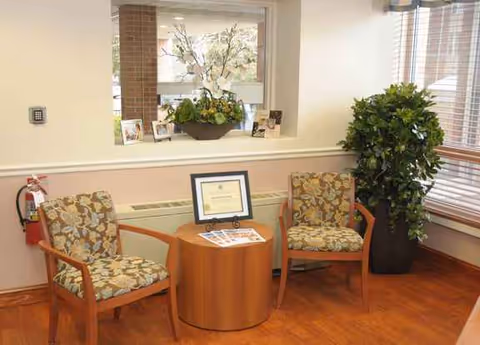 Two patterned chairs flank a small round table with a framed certificate in a waiting area.
