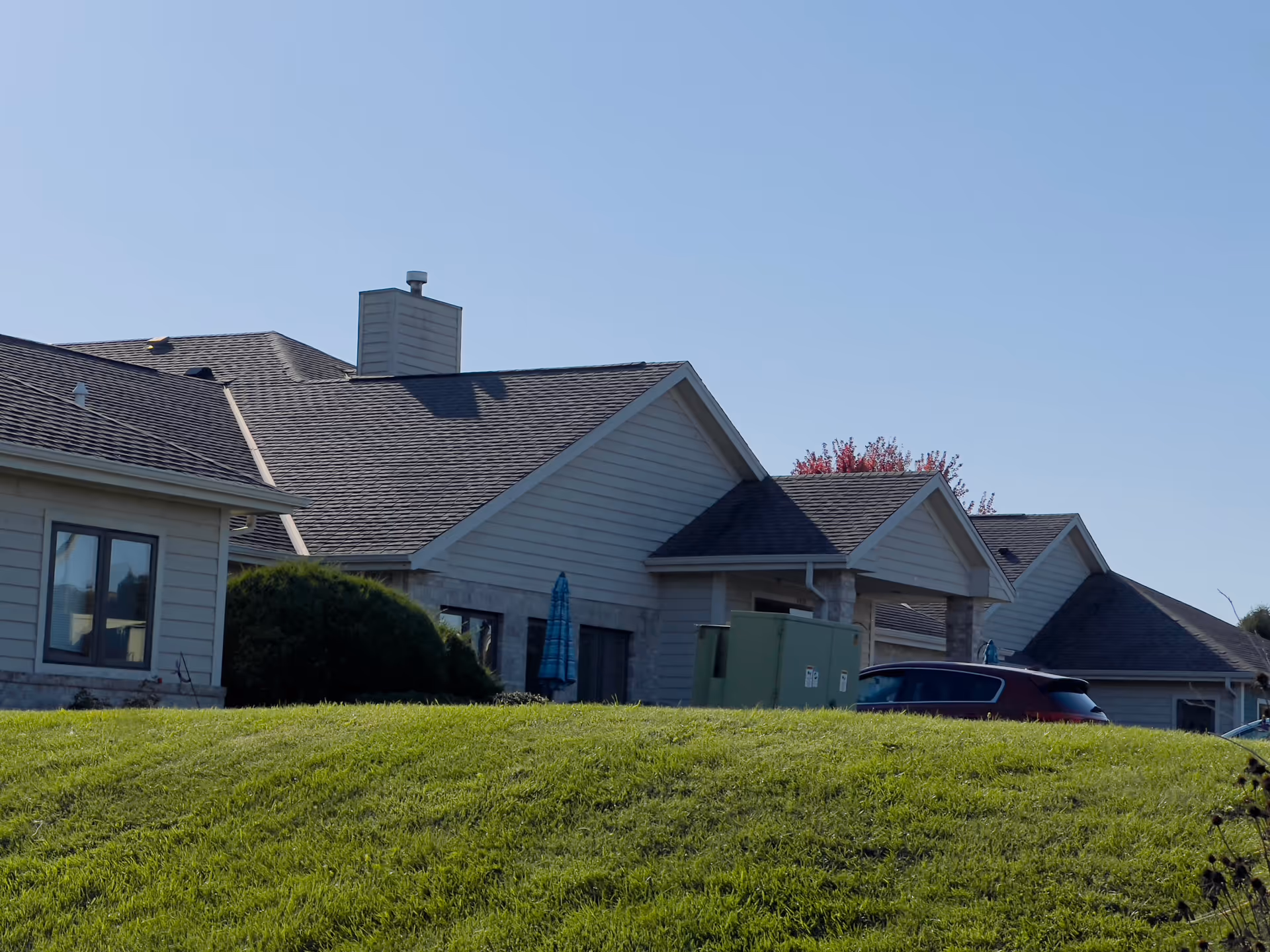 Low-angle view of a single-story assisted living building with pitched roofs, a green lawn in the foreground and a parked car.