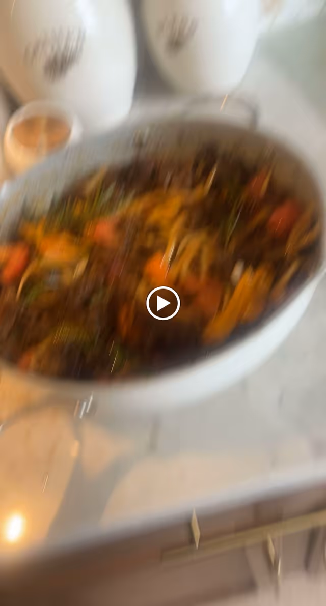 A close-up view of a bowl filled with a colorful cooked dish containing vegetables and possibly meat, placed on a kitchen countertop with some containers in the background.