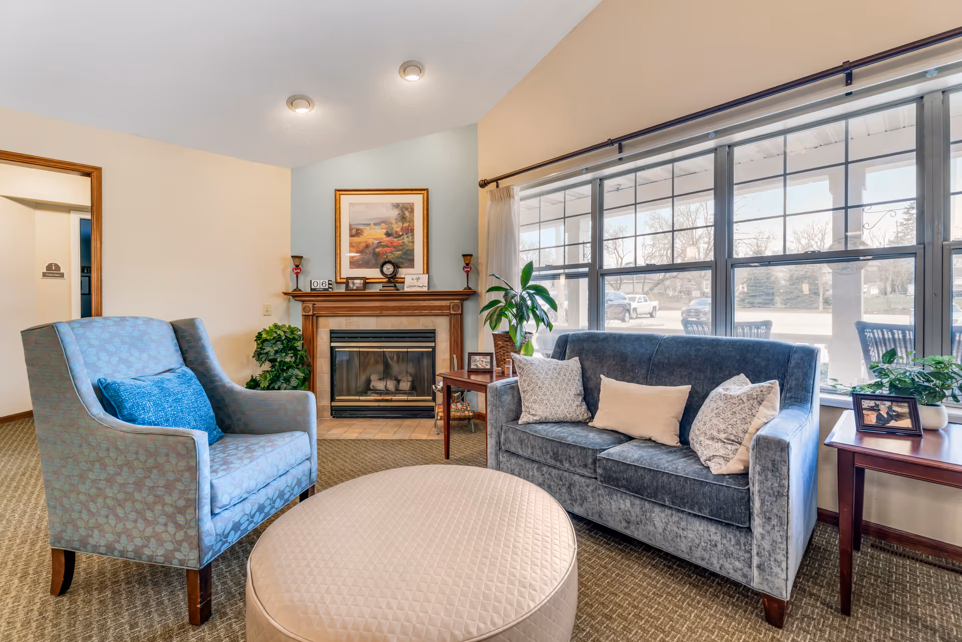 Cozy sitting area with an armchair, a sofa, an ottoman, a fireplace, and large windows overlooking the street.