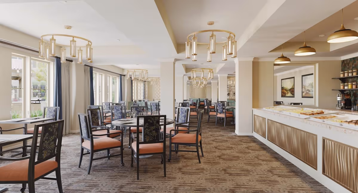 Bright dining room with round tables, cushioned chairs, large windows, chandeliers, and a buffet counter.