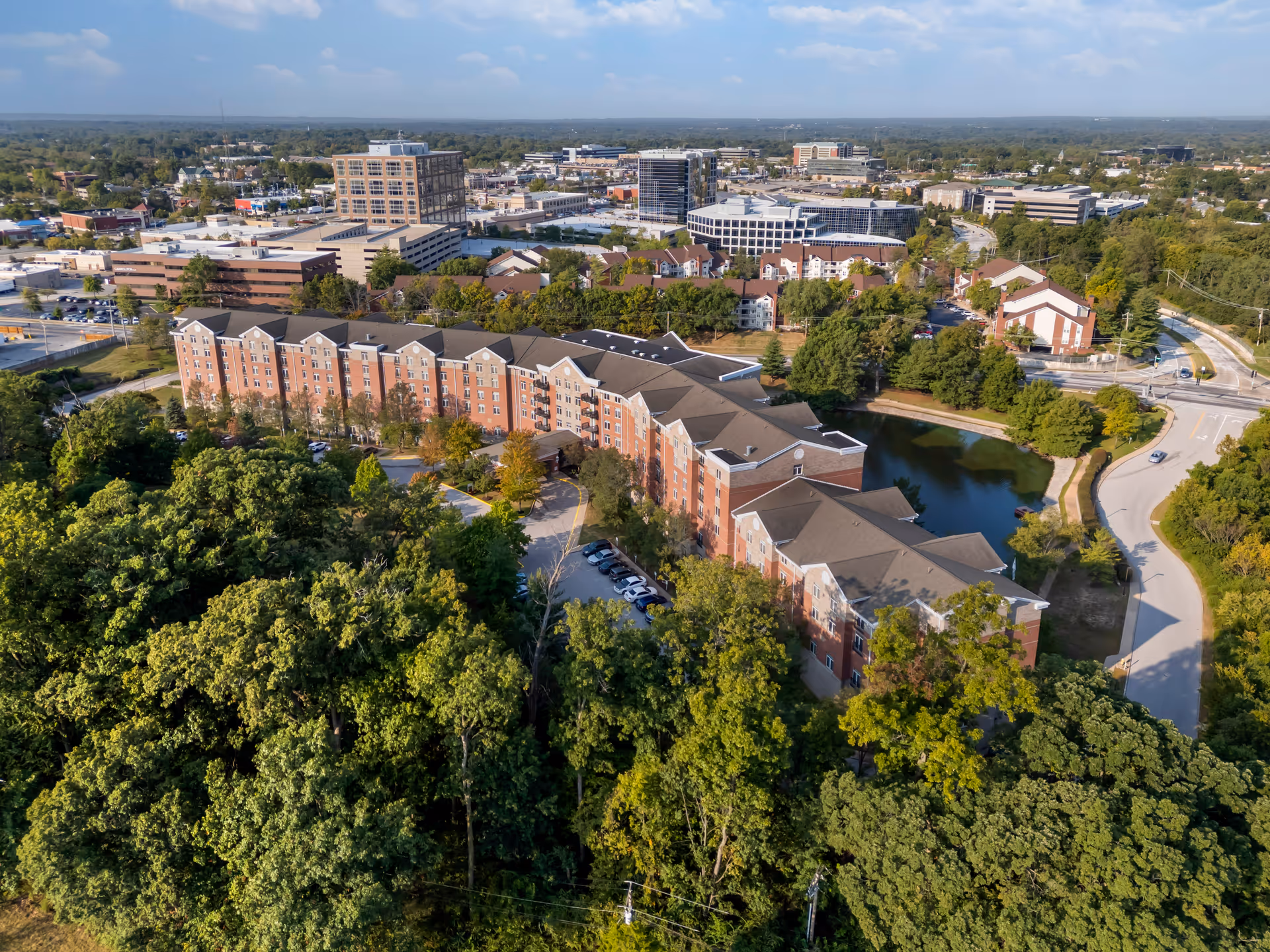 Aerial view of Brookdale Creve Coeur campus with brick buildings, a pond, and surrounding trees.