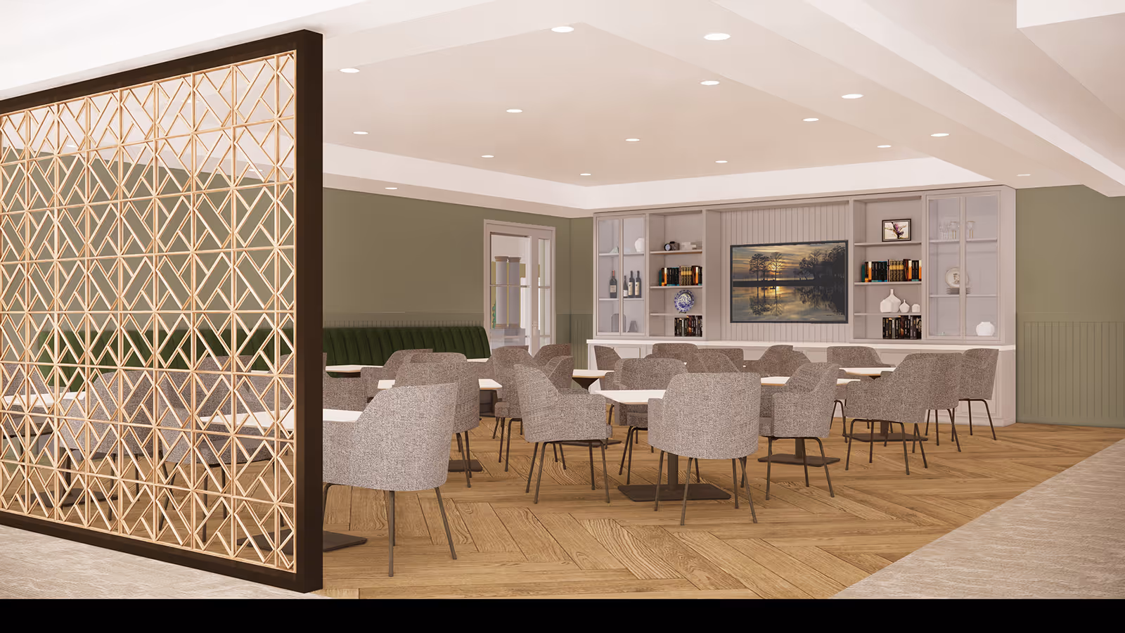 A spacious dining room with multiple tables and gray upholstered chairs arranged neatly. The room features a decorative wooden partition on the left side, green walls with white trim, and a built-in shelving unit on the far wall displaying books, decorative items, and a large framed picture of a sunset over a lake. The floor has a light wood herringbone pattern, and the ceiling is white with recessed lighting.