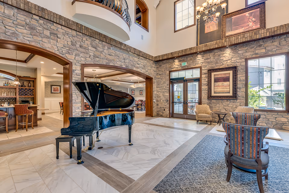 Spacious two-story lobby with a grand piano, seating areas, stone walls, and a bar visible through an archway.
