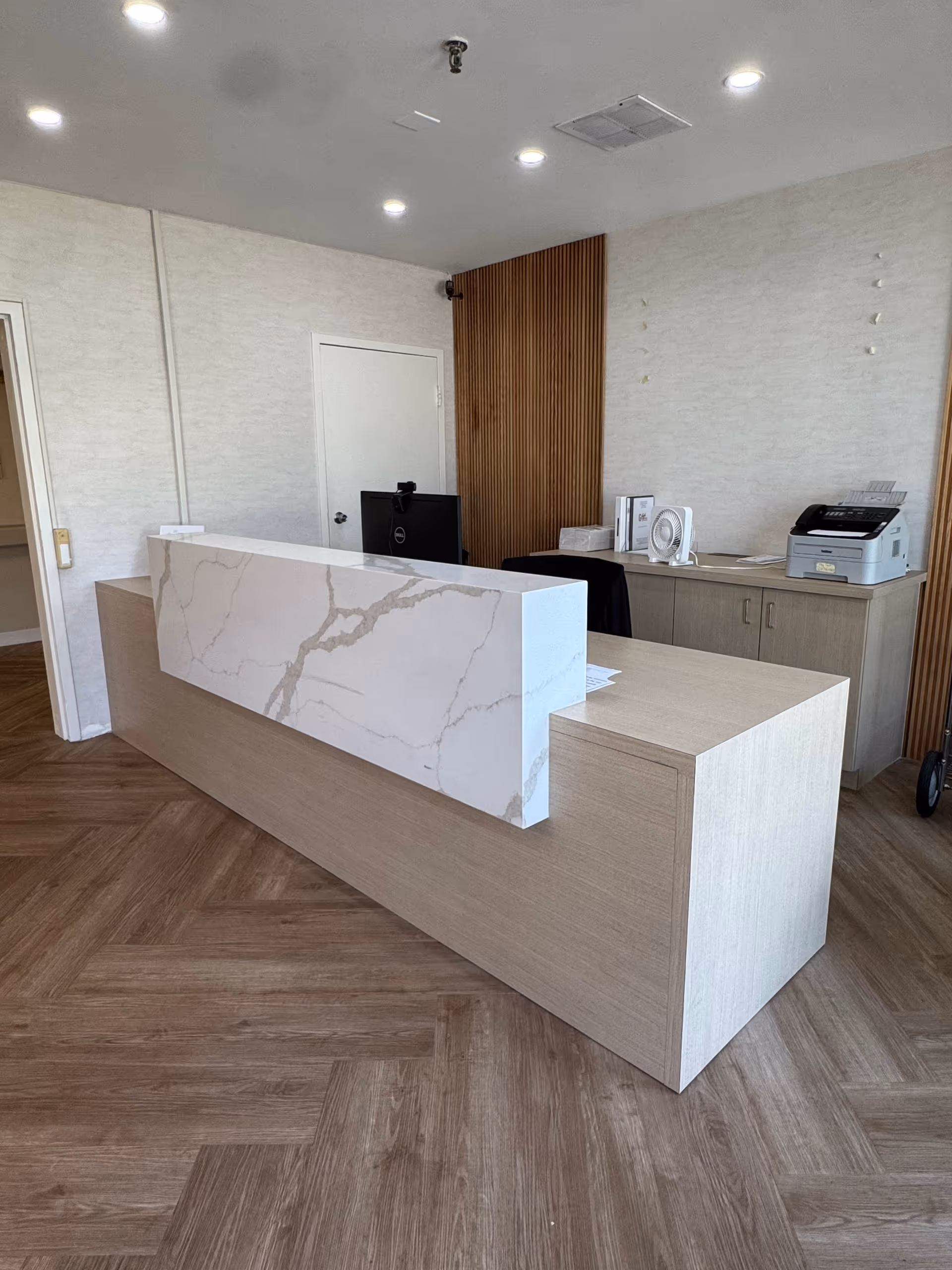 Modern reception desk and check-in area with a marble-faced counter, wood cabinetry, and office equipment.