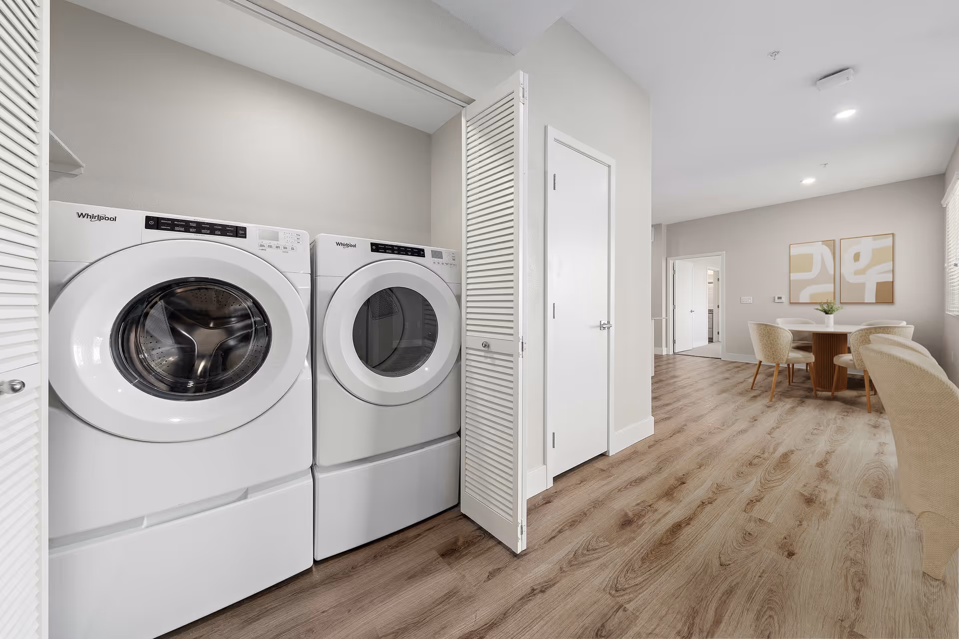 Open closet with a white Whirlpool washer and dryer beside a hallway leading to a dining area with a round table and chairs.