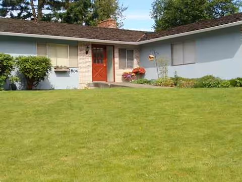 A single-story building with a red front door and a well-kept lawn.