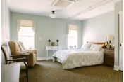 A furnished senior living bedroom with a bed, two windows, and seating.