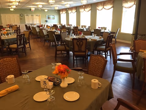 Spacious dining room with multiple round tables set for service, chairs, and floral centerpieces.