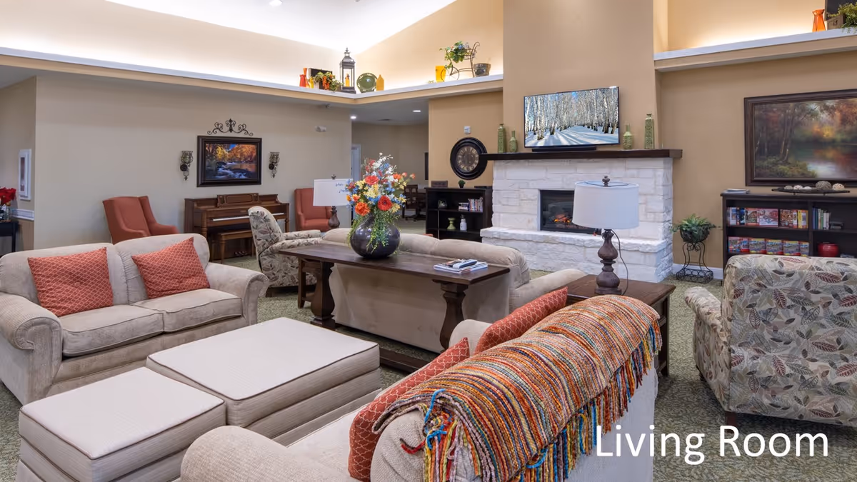 Cozy furnished living room with sofas, armchairs, a fireplace, TV, piano and floral centerpiece on a central table.