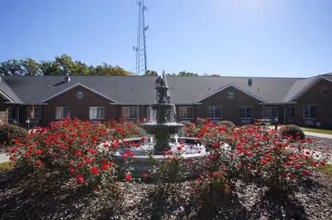 Brick senior living facility with a central fountain surrounded by red rose bushes.