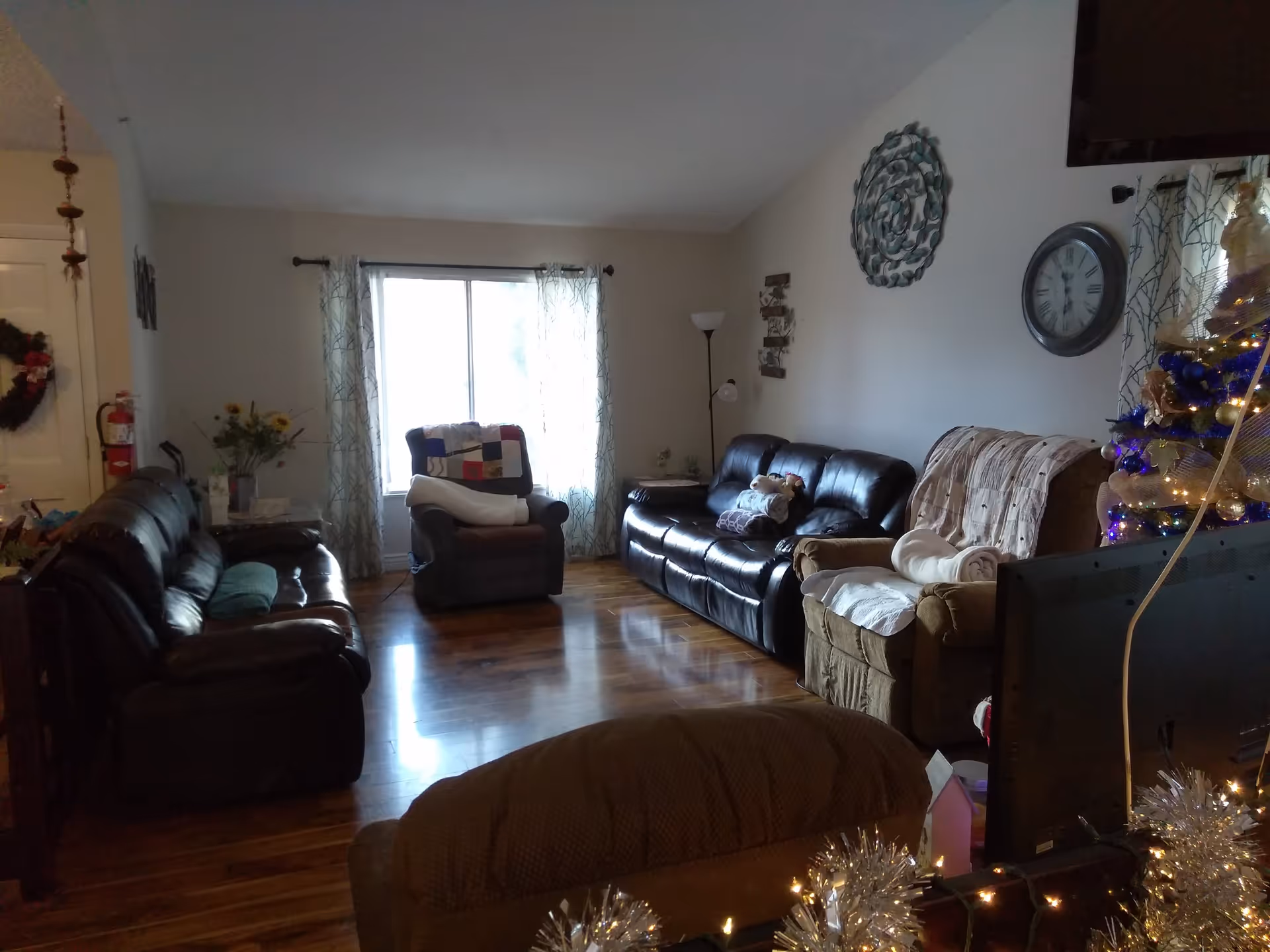 Cozy living room with leather sofas and armchairs, a window with curtains, wall decor and a decorated Christmas tree.