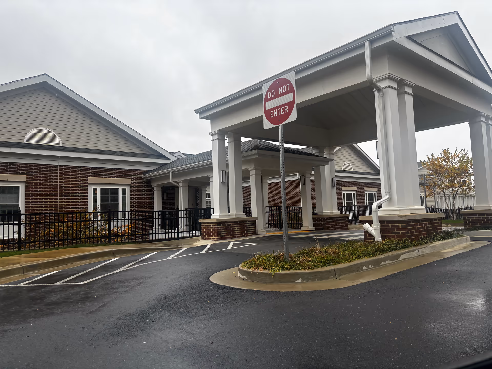Exterior view of HarborChase of Olney showing a covered entrance with white columns and brick base, a 'Do Not Enter' sign, and a paved driveway on a cloudy day.