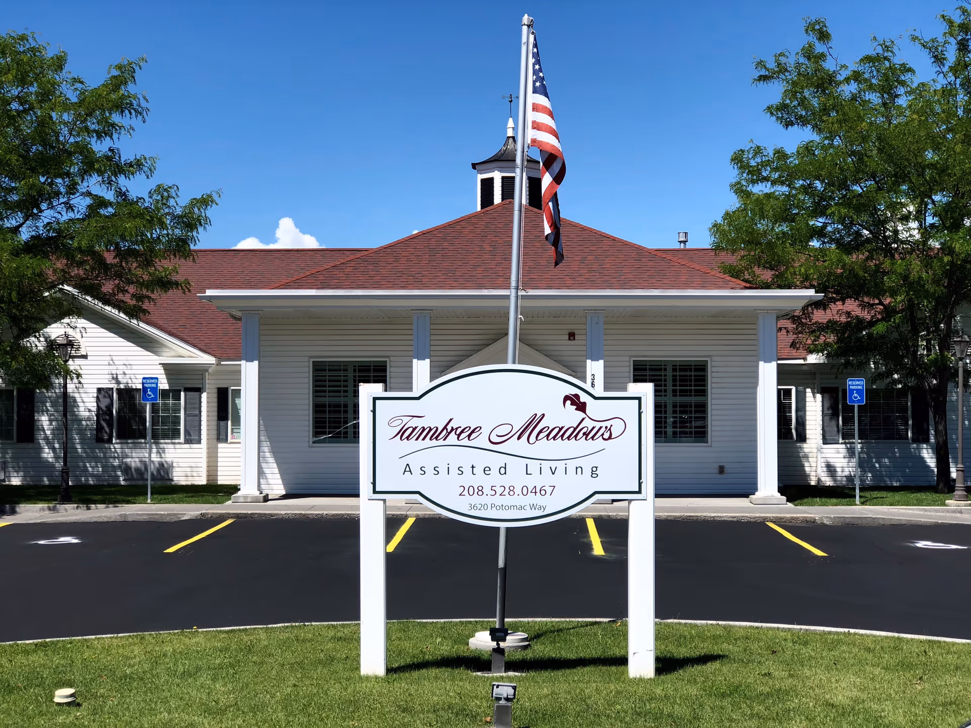 Front entrance of Tambree Meadows Assisted Living with a large sign and an American flag in front of a white single-story building.