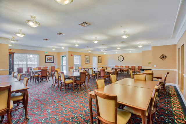 Spacious dining room with multiple wooden tables and upholstered chairs on a patterned carpet under ceiling lights.