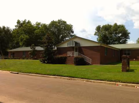 Brick senior care home exterior with awning, steps, and well-kept lawn.