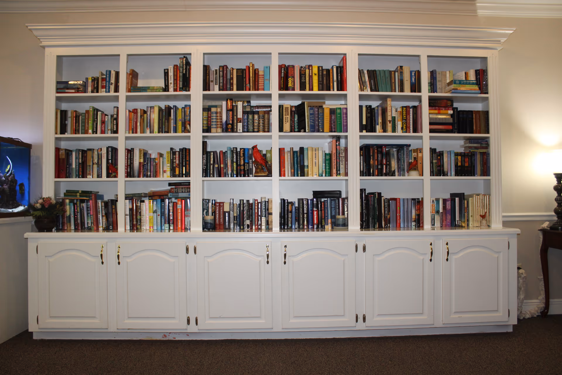 White built-in bookshelf with multiple shelves filled with books against a wall in a room.