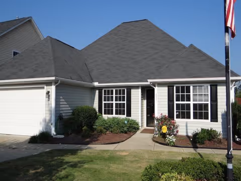 Front exterior of a single-story building with shrubs, a walkway, a garage, and an American flag.