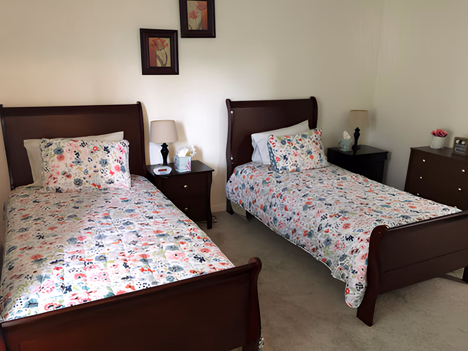 Two twin beds with floral quilts in a neatly arranged bedroom with nightstands, lamps, and a dresser.