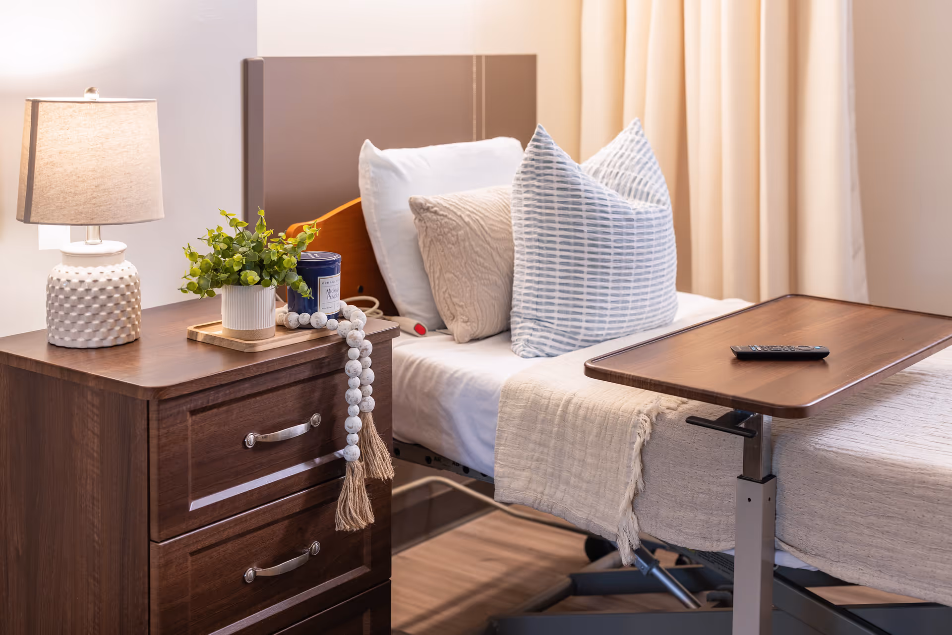 A cozy senior living room setup with a bed, bedside table, lamp, and decorative items.