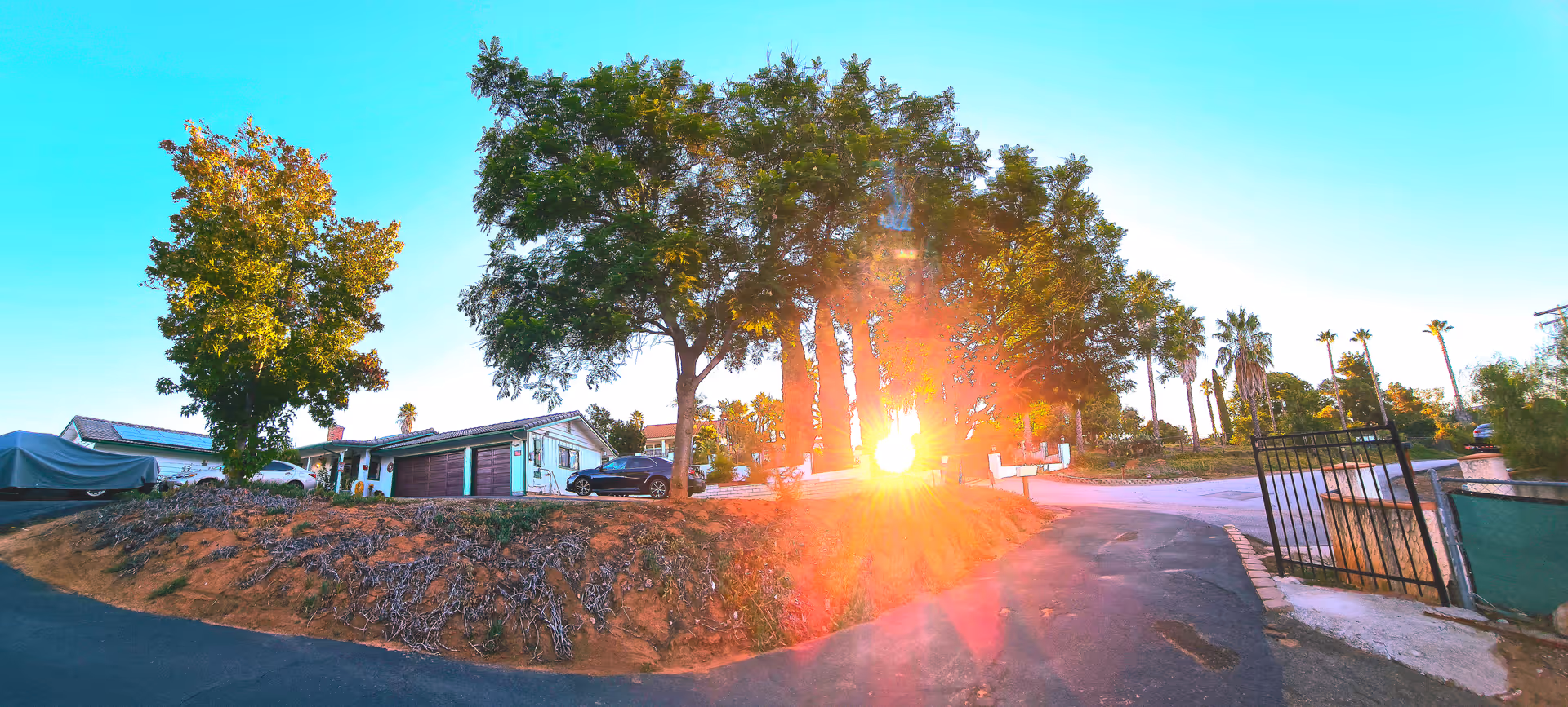 Single-story house-like building with a driveway, large trees, and bright sun glare near the entrance.