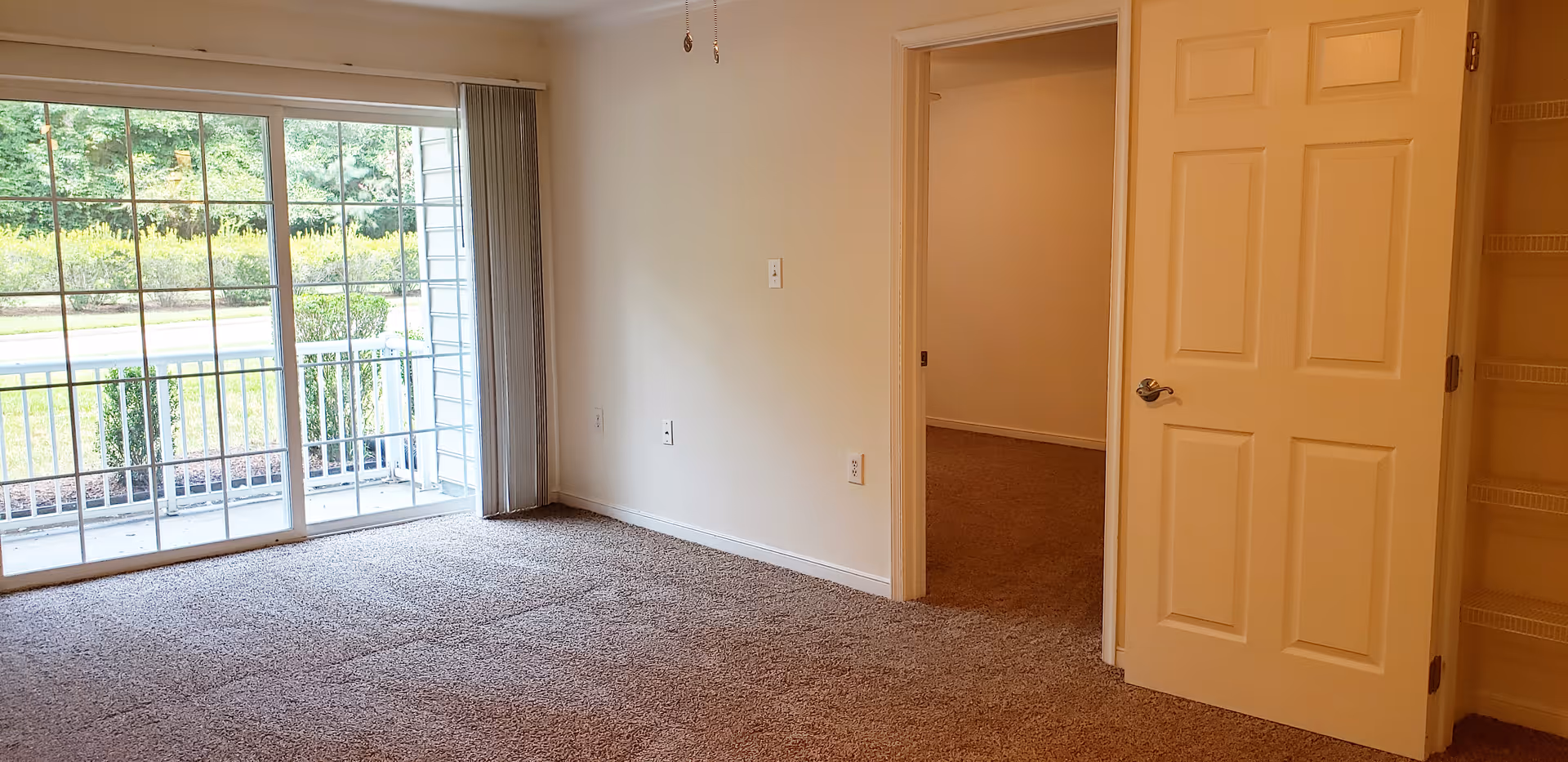 Carpeted living room with sliding glass doors to a small balcony and an open doorway to another room.