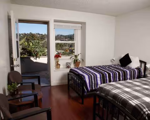 Two twin beds in a bright shared bedroom with a doorway to a small patio.