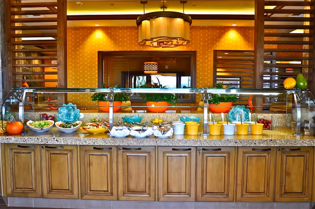 A buffet-style serving counter with bowls of salads and garnishes under a glass sneeze guard in a warmly lit dining area.