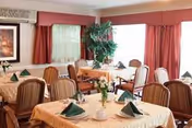 Dining room with round tables, red drapes, green folded napkins, and a potted plant.