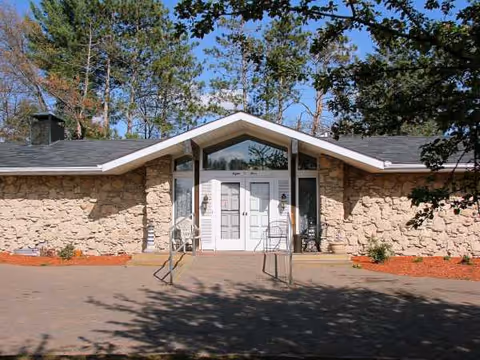 Front entrance of a stone-clad senior living facility with double doors and a pitched roof.