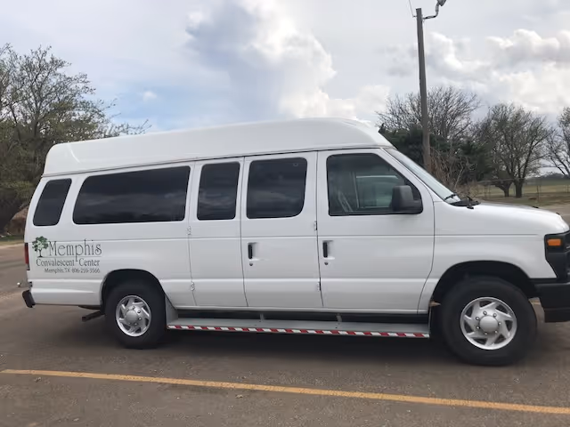 White passenger van parked in an outdoor parking lot with the logo and name 'Memphis Convalescent Center' on the side. The sky is partly cloudy and there are trees in the background.
