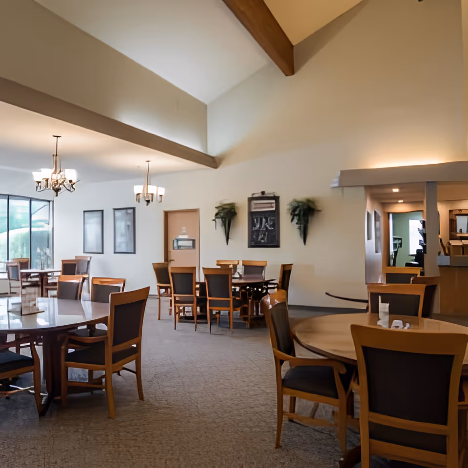 Spacious dining room with round wooden tables and chairs under a vaulted ceiling with exposed beams and chandeliers.