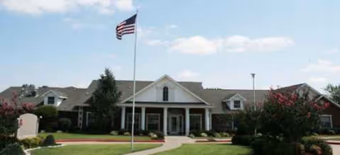 Single-story senior living facility with a flagpole and manicured landscaping at the entrance.