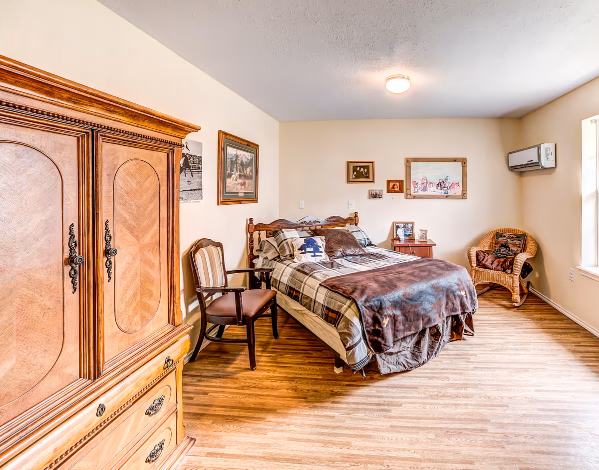 Sunlit bedroom with a double bed, wooden armoire, chairs, and framed artwork on the walls.