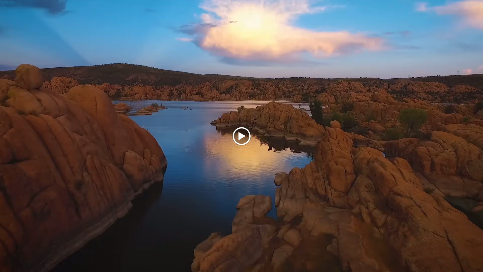 Rocky lake with calm water reflecting a glowing cloud at sunset amid rugged rock formations.