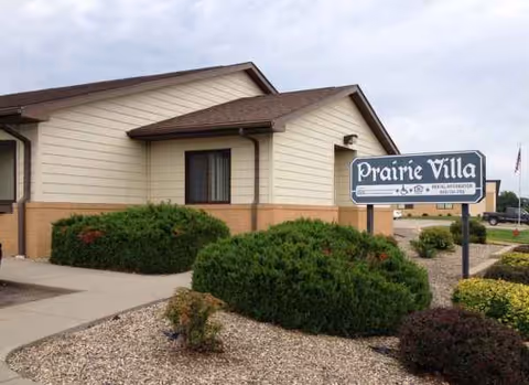 Exterior view of Prairie Villa senior living facility with sign and landscaped bushes.