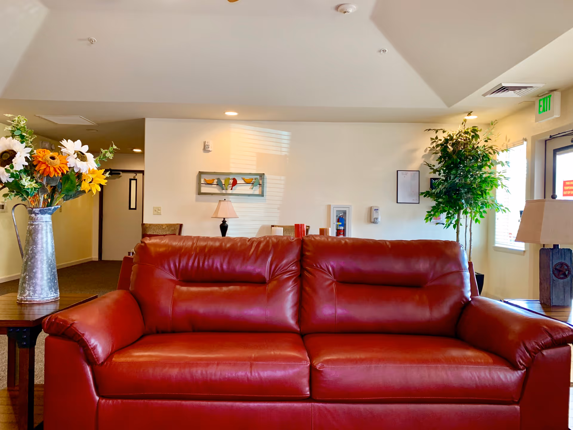 Red leather sofa in a bright common sitting area with a floral arrangement, lamps, and a potted plant.
