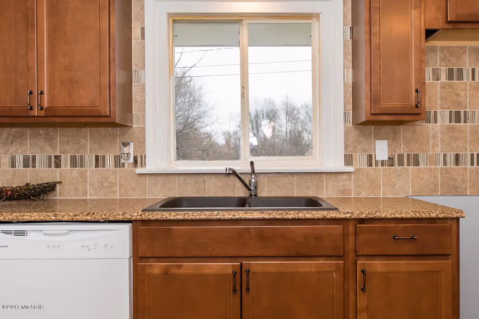 Kitchen sink and countertop with wooden cabinets and a window above.