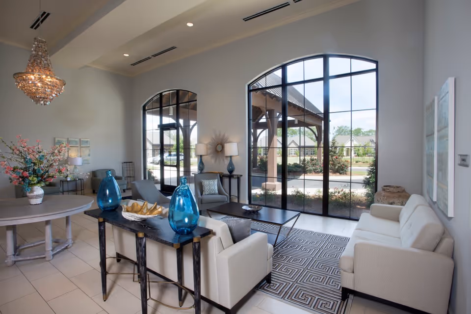 Bright, elegant common living room with sofas, a coffee table, large arched windows, decorative blue vases and a chandelier.