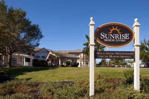 Sunrise Senior Living sign in foreground with campus buildings and green lawn.