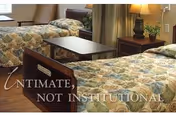 Two twin beds with floral bedspreads, a small table, and a nightstand in a senior living bedroom.